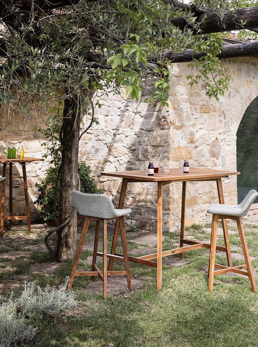 Square wooden bar table from the Gipsy Collection styled in an outdoor hospitality setting with bar stools, ideal for hotels, resorts, and restaurants.