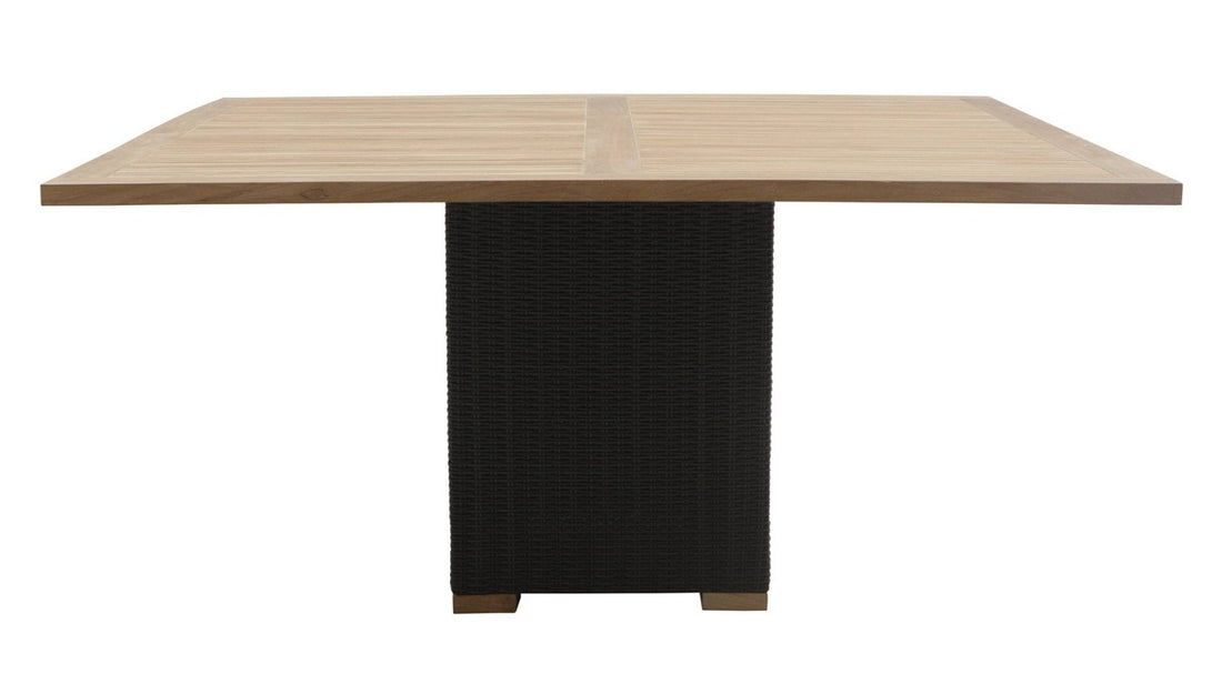 A square dining table with a large square teakwood top and a black wicker fiber base.